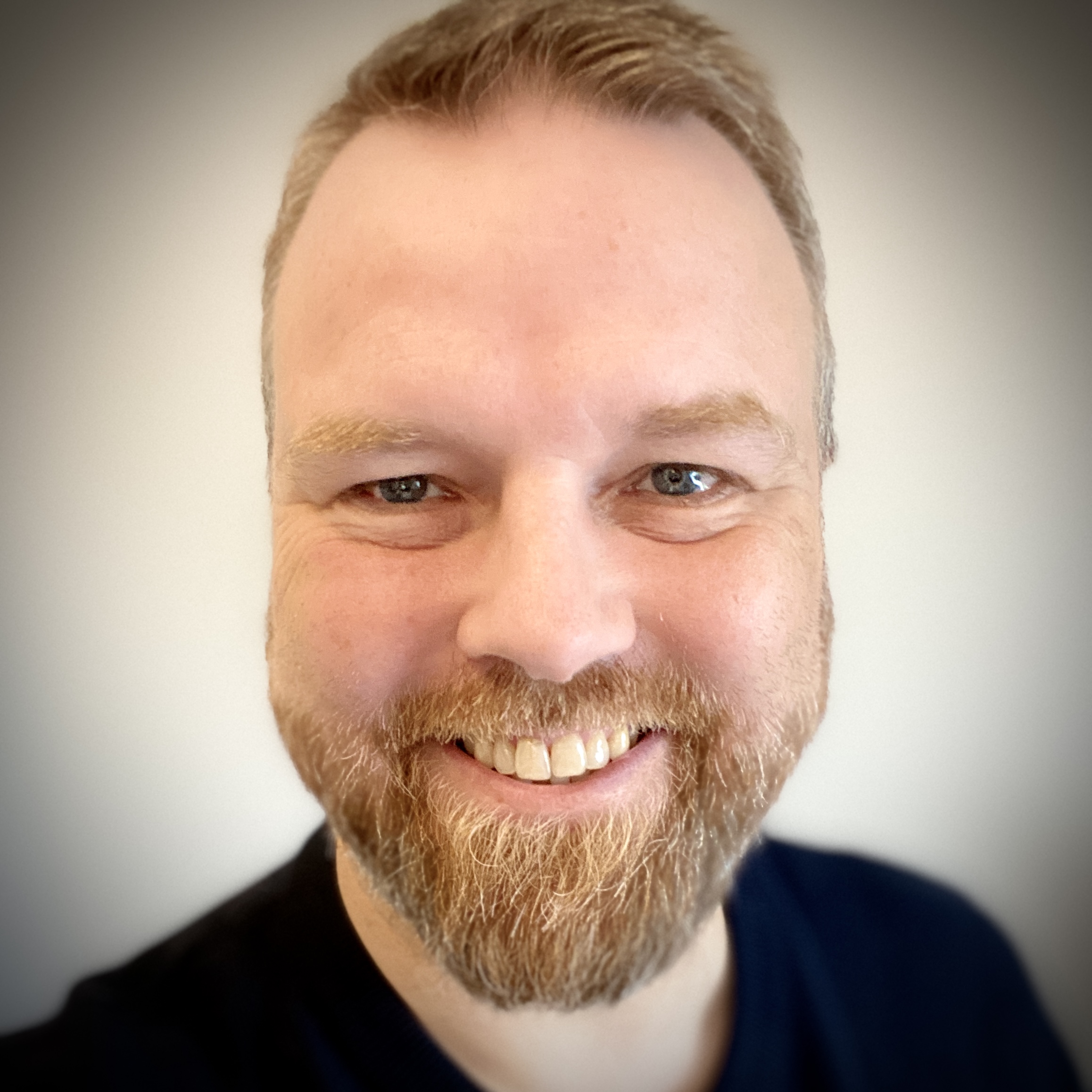 Ein mittelalter Mann mit rotblondem Haar und Vollbart lächelt in die Kamera.