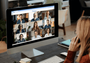 Eine Frau sitzt vor einem Monitor, auf dem eine Videokonferenz mit 9 Personen in Consularia Office läuft.